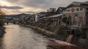 枕崎市のかつお節工場が並ぶ河川と、長年の排水流入で赤褐色に濁る水面のイメージ
